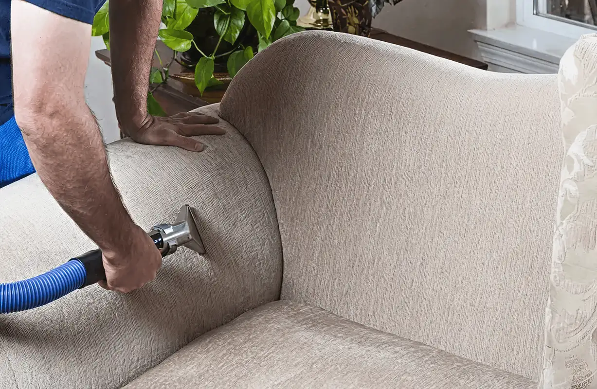 Professional upholstery cleaner deep-cleaning a fabric sofa with a handheld extraction tool and hose, Des Moines, IA.
